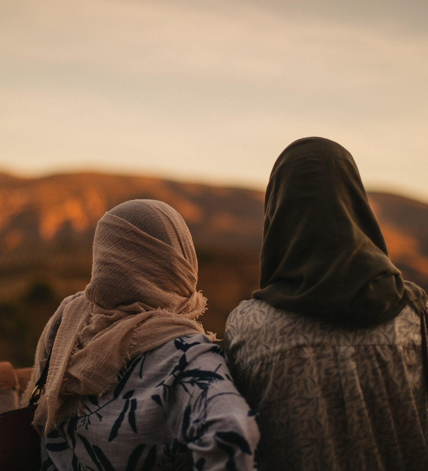 Dos chicas de la comunidad, de espaldas, miran la montaña al atardecer.